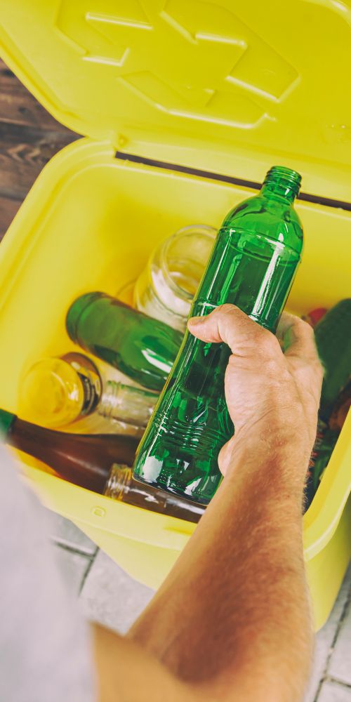 Main déposant une bouteille en verre dans un bac de tri sélectif jaune